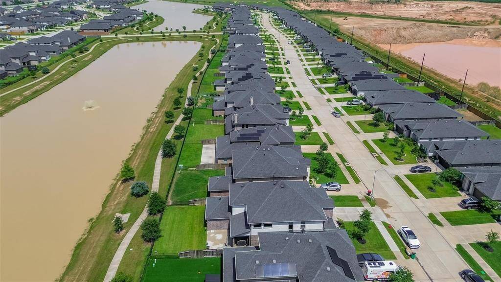 This aerial view showcases a modern suburban neighborhood with neatly aligned homes and well-maintained lawns. The street runs parallel to a scenic waterway, providing a pleasant and serene environment.