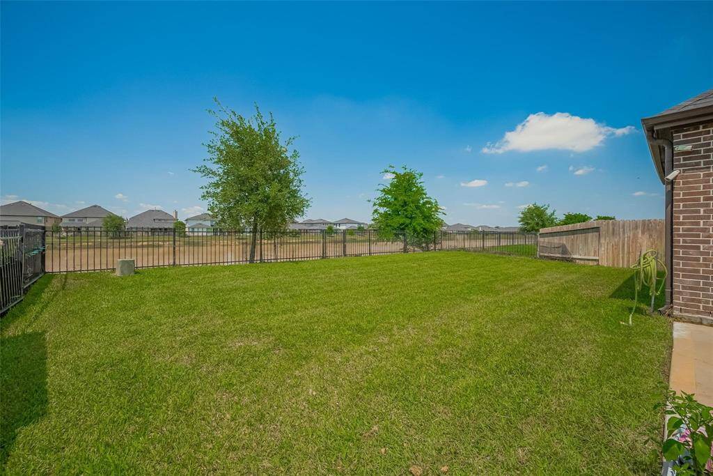 Spacious backyard with a well-maintained lawn, bordered by a metal fence for added security, offering a clear view of neighboring rooftops and open skies, perfect for outdoor activities.