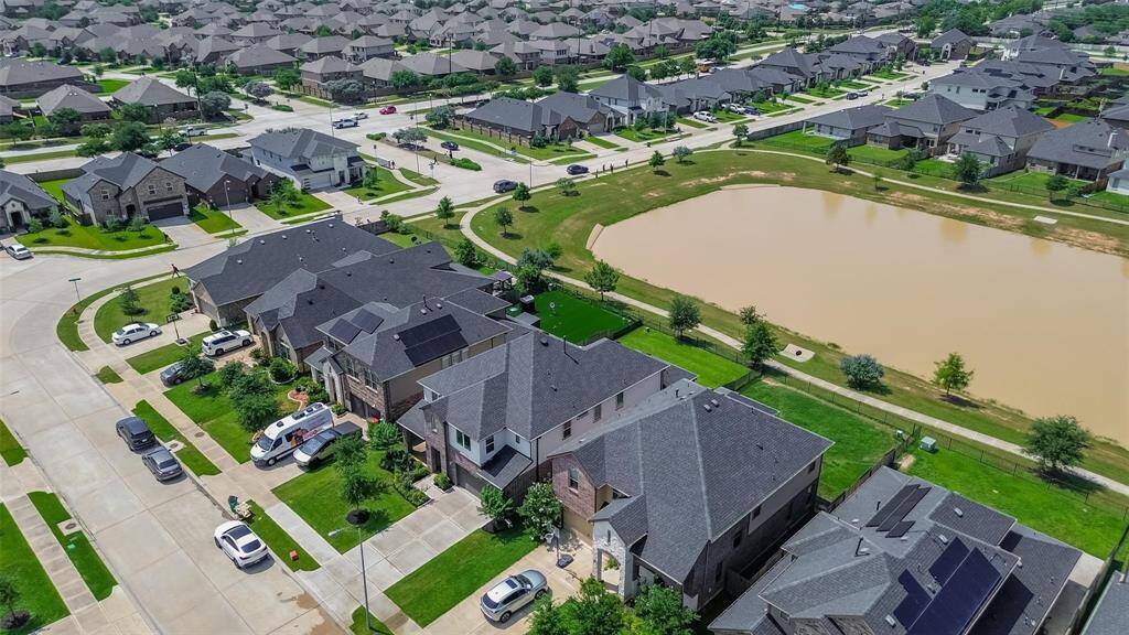 This aerial photo showcases a suburban neighborhood with modern homes, neatly manicured lawns, and a nearby lake. The streets are spacious, and the area appears tranquil and well-maintained, ideal for families.
