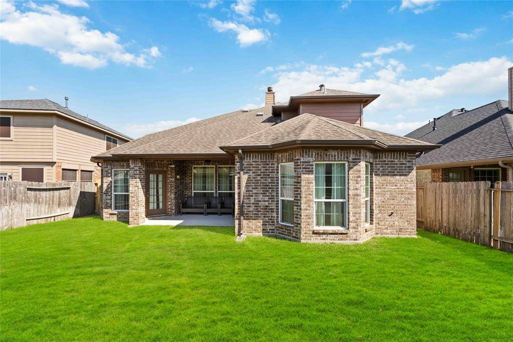A straight-on view of the back of the home from the backyard showcases the full brick and stone exterior, covered patio, and architectural details that make this space truly stand out.
