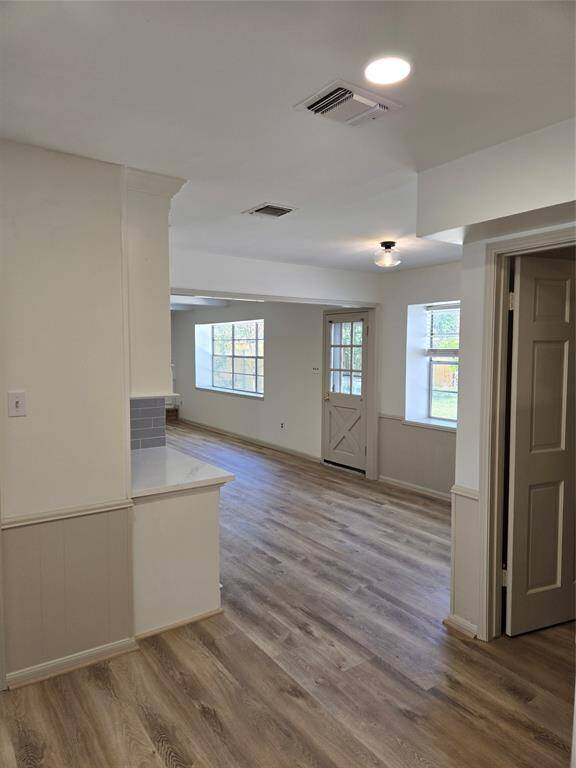 This photo showcases a bright, open living area with wood flooring and neutral walls. The space features large windows for natural light, a side door, and an adjoining kitchen counter with light tile backsplash.
