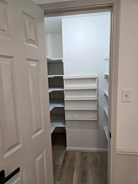 This photo shows a pantry with ample shelving for storage. It features wooden flooring and a white door, providing a clean and organized space.