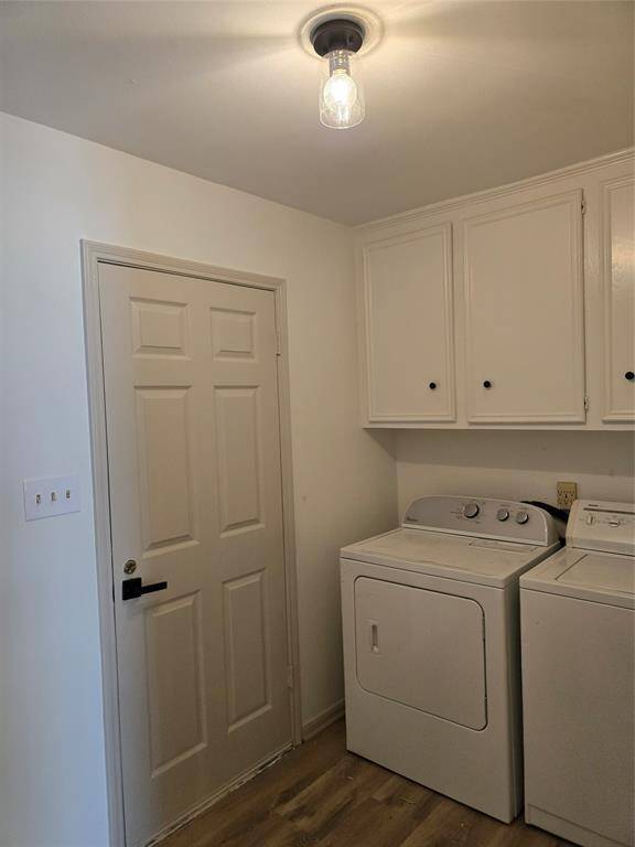 This photo shows a laundry room with a washer and dryer, white cabinetry for storage, and a door. The space is well-lit with a simple ceiling light and features light-colored flooring.