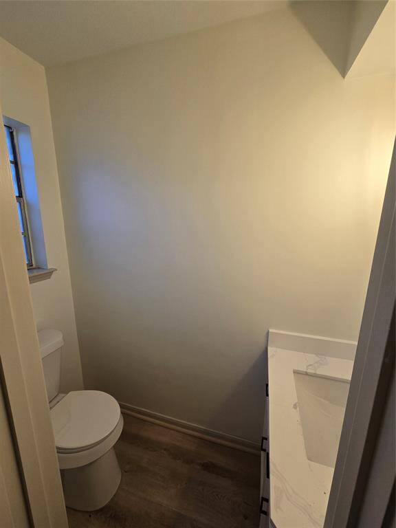 This photo shows a compact bathroom with a modern design. It features a toilet and a sleek countertop with a built-in sink. The walls are painted a light color, and there's a small window providing natural light, complemented by wood-look flooring.