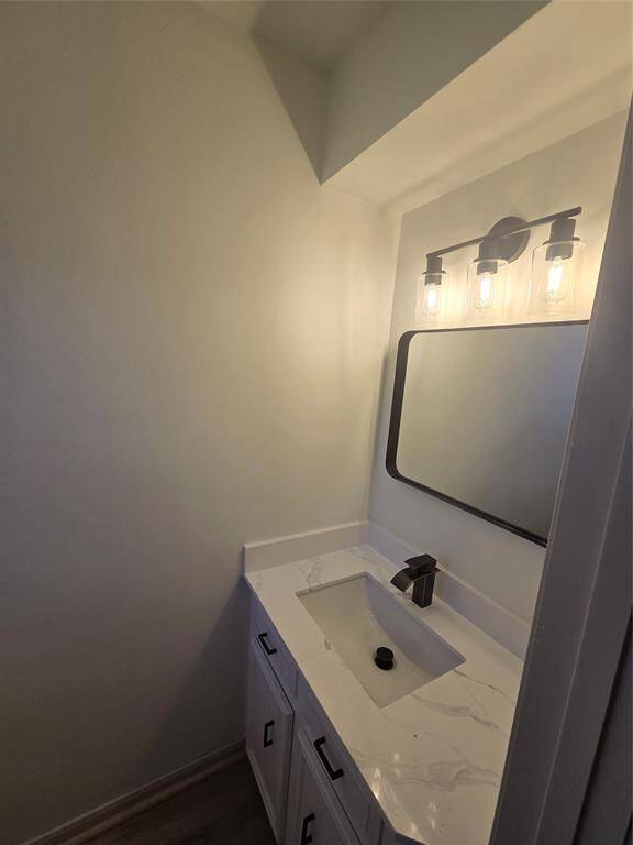 A modern bathroom with a sleek vanity featuring a marble countertop and an undermount sink. The space is well-lit with a stylish three-bulb light fixture above a rectangular mirror.