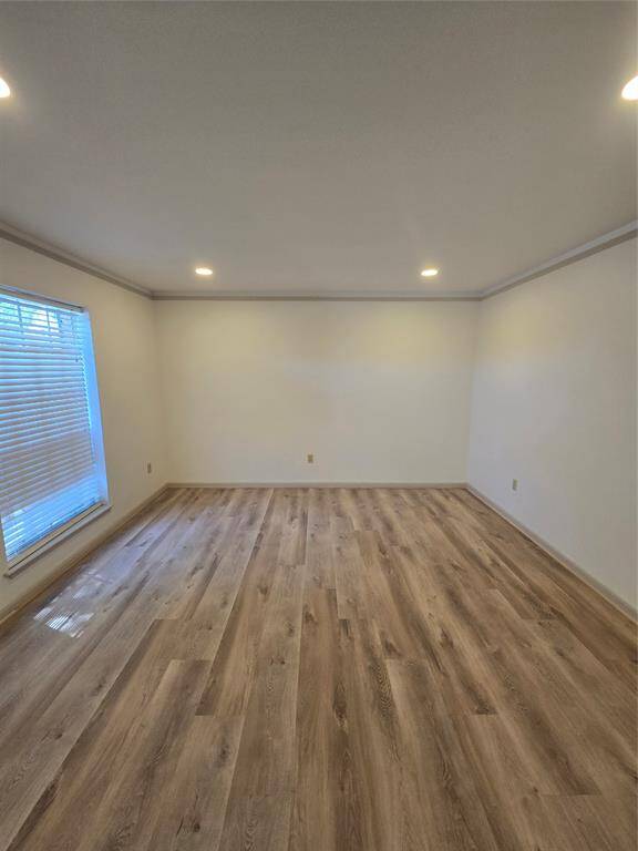 This room features light wood flooring, neutral walls, and recessed lighting. A large window with blinds provides natural light. Ideal for a cozy living space or bedroom setting.