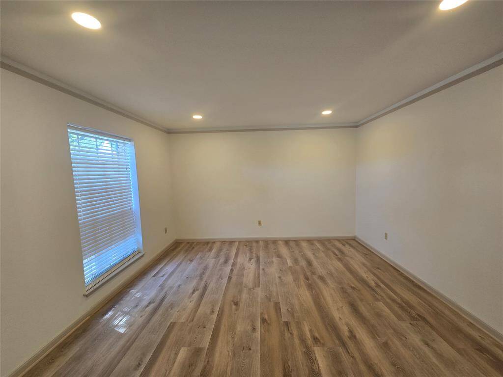 Bright, spacious room with recessed lighting, wood flooring, and a large window with blinds, creating a warm and inviting atmosphere.