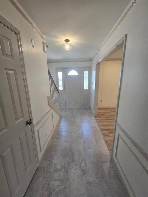 Bright entryway with tiled flooring, leading to a staircase and an adjoining room with wood flooring. Features a glass-paneled front door and elegant molding on the walls.