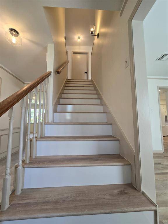 This photo shows a bright, inviting staircase with wooden steps and white railings, leading to a closed door at the top. The space features modern lighting and a neutral color palette, creating a clean and welcoming atmosphere.
