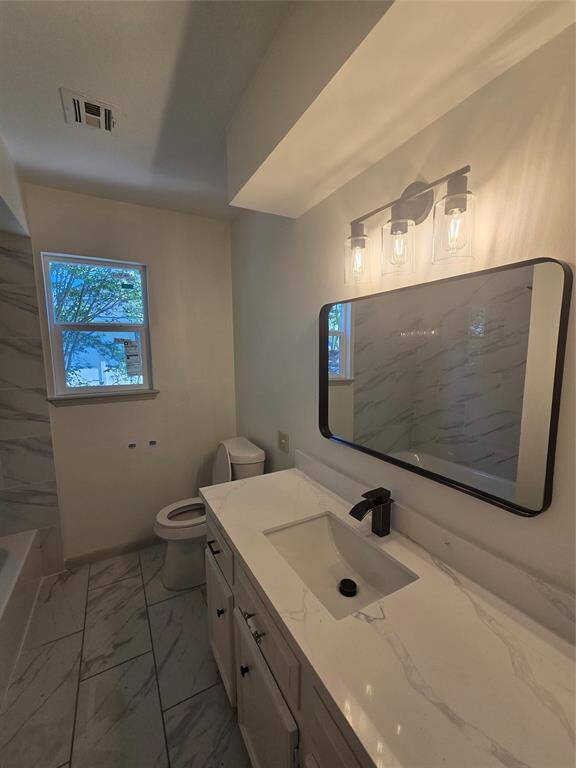Modern bathroom featuring marble-patterned tiles, a sleek vanity with a contemporary faucet, and stylish lighting. Natural light from the window enhances the clean, fresh ambiance.