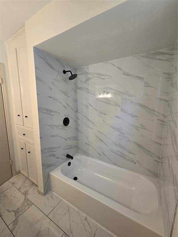 This bathroom features a modern bathtub with elegant marble-patterned tiles and matte black fixtures. It includes built-in shelving for storage and a sleek, contemporary design.
