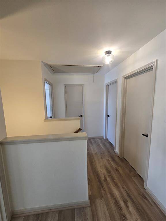 This photo shows a hallway with light wood flooring and white walls. There are three doors and a ceiling light fixture, providing a clean and simple design.