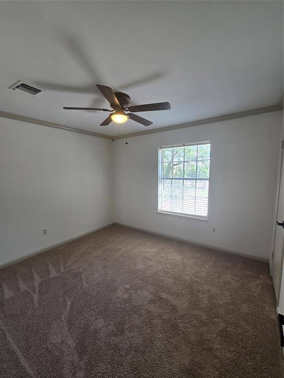 This is a bright, carpeted room with neutral walls, featuring a ceiling fan and a large window offering natural light. Ideal for a cozy bedroom or home office.