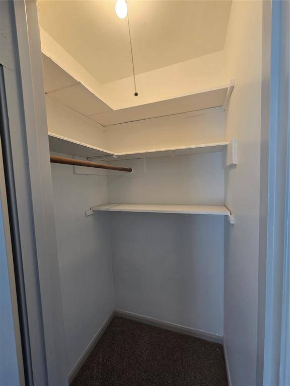This is a compact walk-in closet with a hanging rod, two shelves, and overhead lighting. It's perfect for organizing clothes and accessories efficiently.
