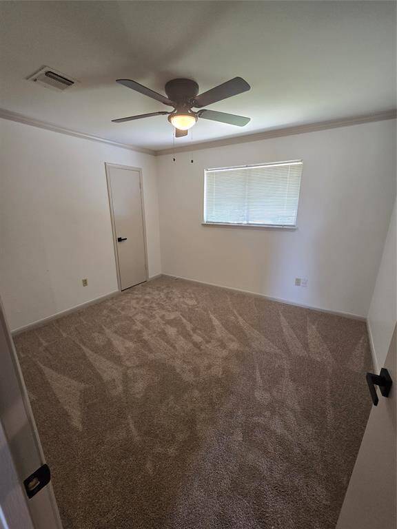 This is a cozy, carpeted bedroom with a ceiling fan, a window providing natural light, and a door. The neutral walls offer a blank canvas for personalization.