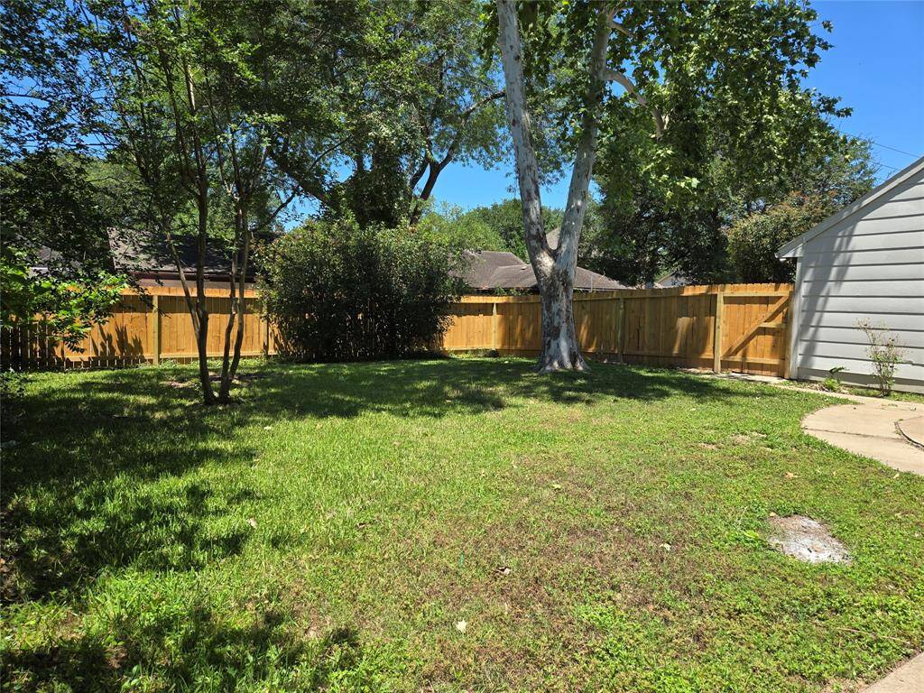 A spacious backyard with lush green grass, mature trees, and a wooden fence, offering privacy and a serene outdoor space. Ideal for relaxation or entertaining.