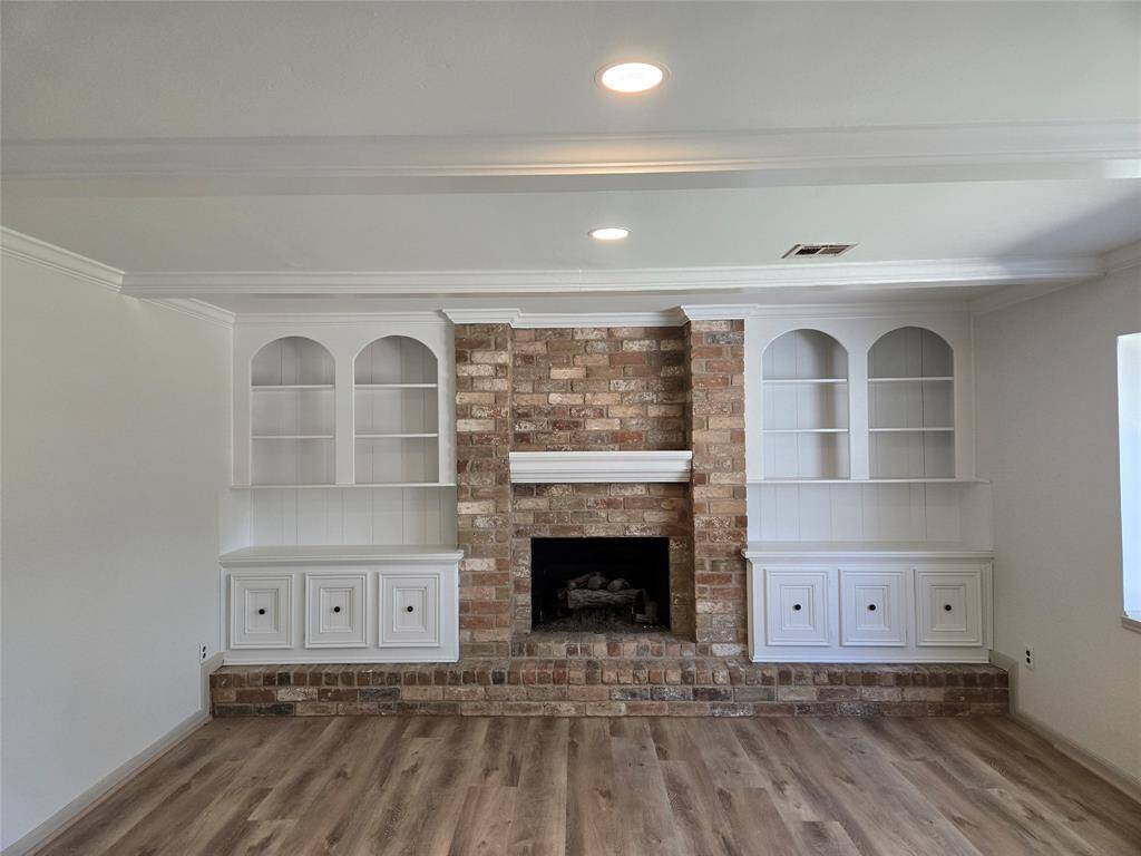 This room features a cozy brick fireplace flanked by built-in shelves and cabinets. The space is bright with recessed lighting and has a warm, wood-look floor, creating a welcoming atmosphere.
