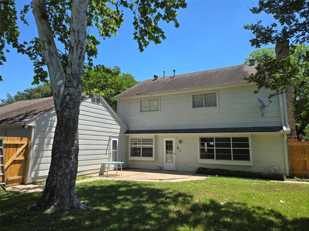 This photo showcases a two-story home with a spacious backyard, featuring a large tree providing shade. The exterior is light-colored with a pitched roof and several windows, offering a bright and inviting atmosphere. A wooden fence adds privacy, and there's a small patio area perfect for outdoor activities.