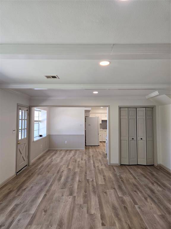 This photo showcases a bright, open living area with laminate wood flooring, recessed lighting, and a neutral color palette. The space features a door with a window, a large closet with double doors, and an adjacent kitchen area.