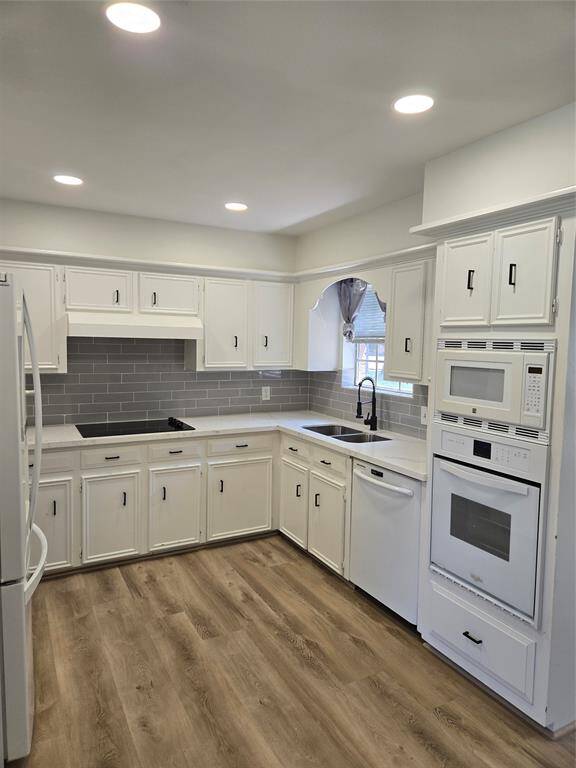 This kitchen features a modern design with white cabinetry and sleek gray subway tile backsplash. It includes built-in appliances, a spacious countertop, and wood-look flooring, creating a bright and inviting space.