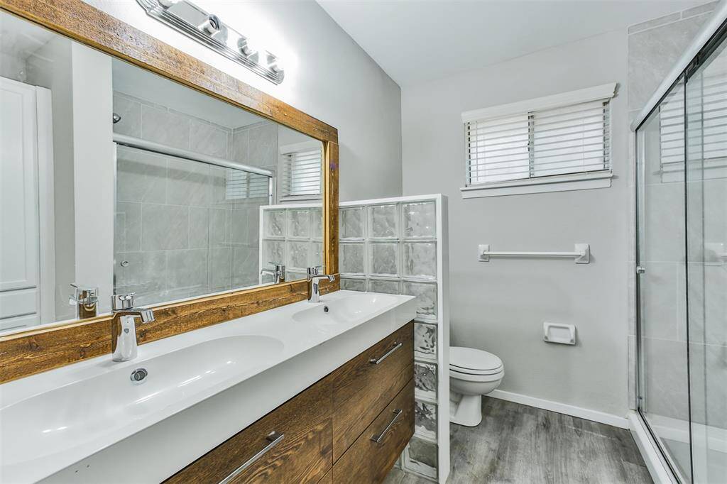 This bathroom features a modern double vanity with a large wooden-framed mirror, stylish light fixtures, and a glass-enclosed shower. The neutral tones and sleek finishes create a clean, contemporary look.
