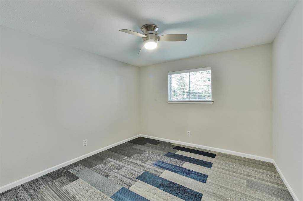 This is a bright, modern bedroom featuring a ceiling fan, a window with natural light, and unique patterned flooring. The neutral wall color enhances the room's spacious feel.