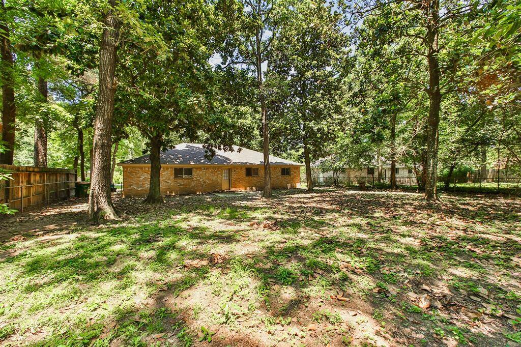 This photo showcases a single-story brick home set in a spacious backyard with mature trees, providing ample shade and a sense of privacy. The large, fenced yard is ideal for outdoor activities and gatherings.