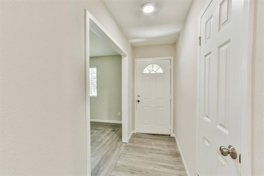 Bright and welcoming entryway with light-colored walls and flooring. Features a front door with a window and a side room visible through an open doorway.