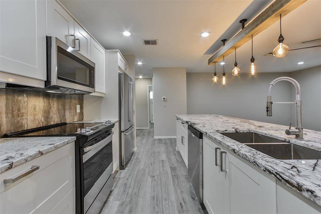This modern kitchen features sleek white cabinetry, stainless steel appliances, and a stylish marble countertop island with a double sink. The space is enhanced by contemporary pendant lighting and wood-look flooring, creating a warm and inviting atmosphere.