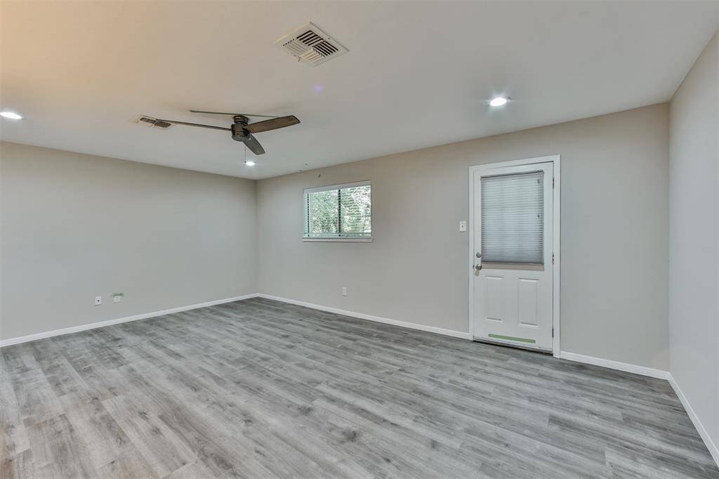 This bright room features modern gray flooring, neutral walls, and a ceiling fan. It includes a window for natural light and a door with a built-in blind, providing easy outdoor access.