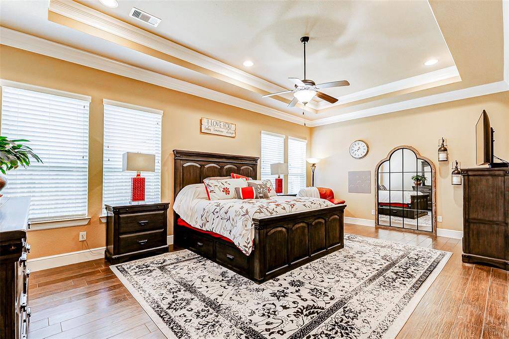 The primary bedroom is a true retreat, offering a serene and luxurious atmosphere. A high tray ceiling, adorned with thick crown molding, adds architectural elegance, while a ceiling fan ensures comfort year-round.