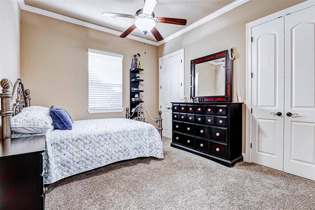 This spacious secondary bedroom offers comfort and style, featuring a high ceiling with crown molding and a ceiling fan for year-round comfort. Plush carpeting underfoot adds warmth and coziness, while a generous double-door closet provides ample storage space.