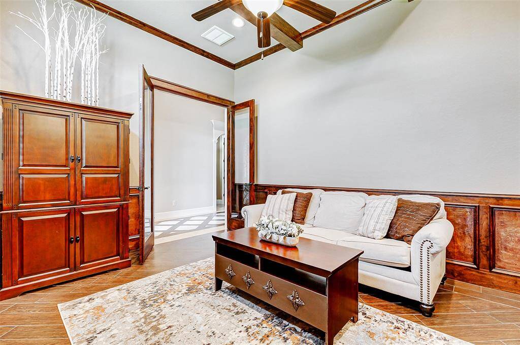 This elegant home office is nestled behind grand French doors, offering both privacy and sophistication. Rich wood-like tile flooring provides warmth and durability, while the walls are accented with handsome wood trim that adds character and charm.