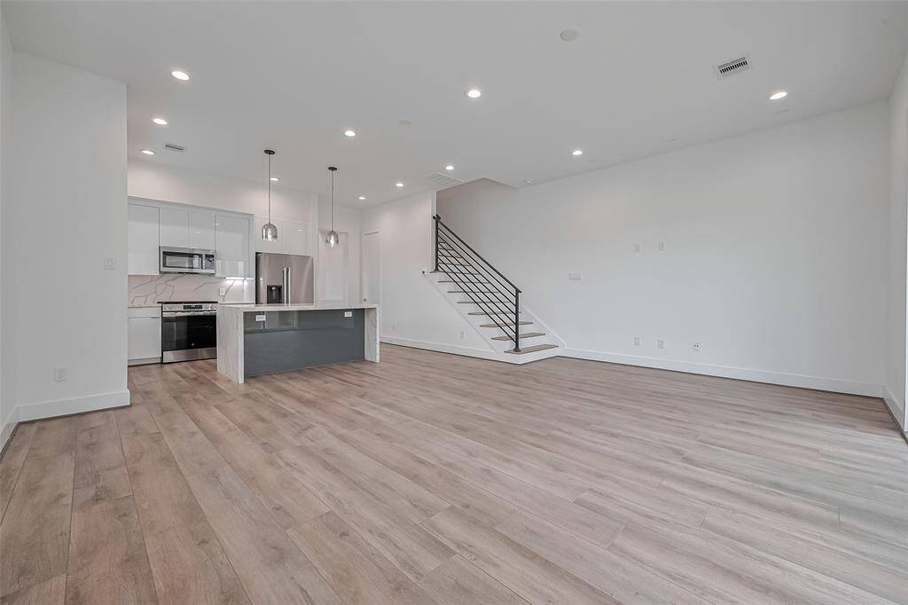 From the living area, the kitchen's clean aesthetic takes center stage, showcasing pristine white cabinetry, polished quartz countertops, and stylish bar seating at the island.