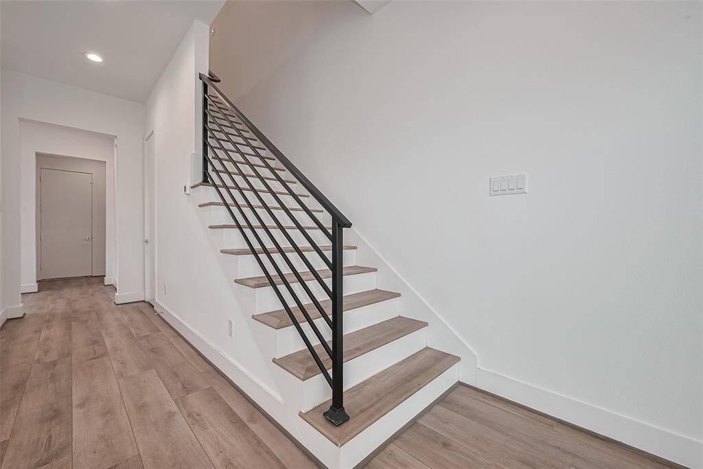 The staircase unites style and structure with rich wood treads that echo the flooring below. A matte black handrail adds a bold contrast and contemporary edge.