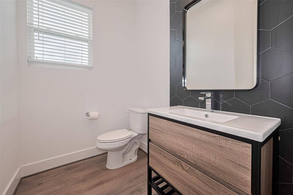 This chic half bath stands out with its black textured accent wall and streamlined vanity. Just outside, a practical nook with hooks, cubbies, and shelving offers a perfect drop zone for everyday essentials.