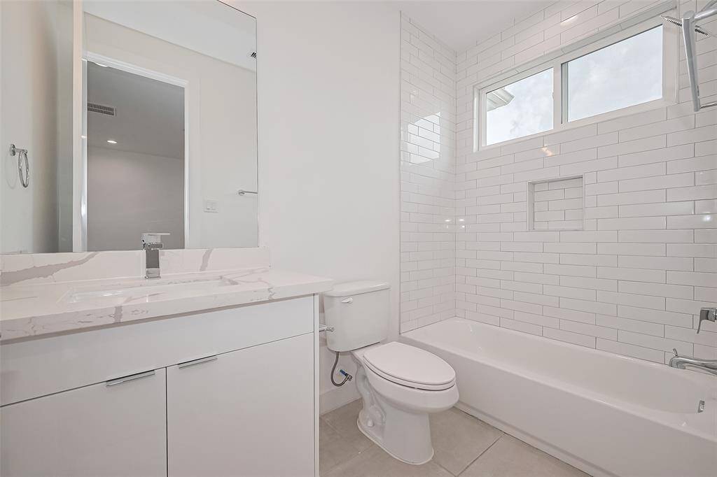 This en suite includes a tub and shower combo, crisp white vanity, large mirror, and stylish modern lighting, delivering spa-like calm in a compact footprint.