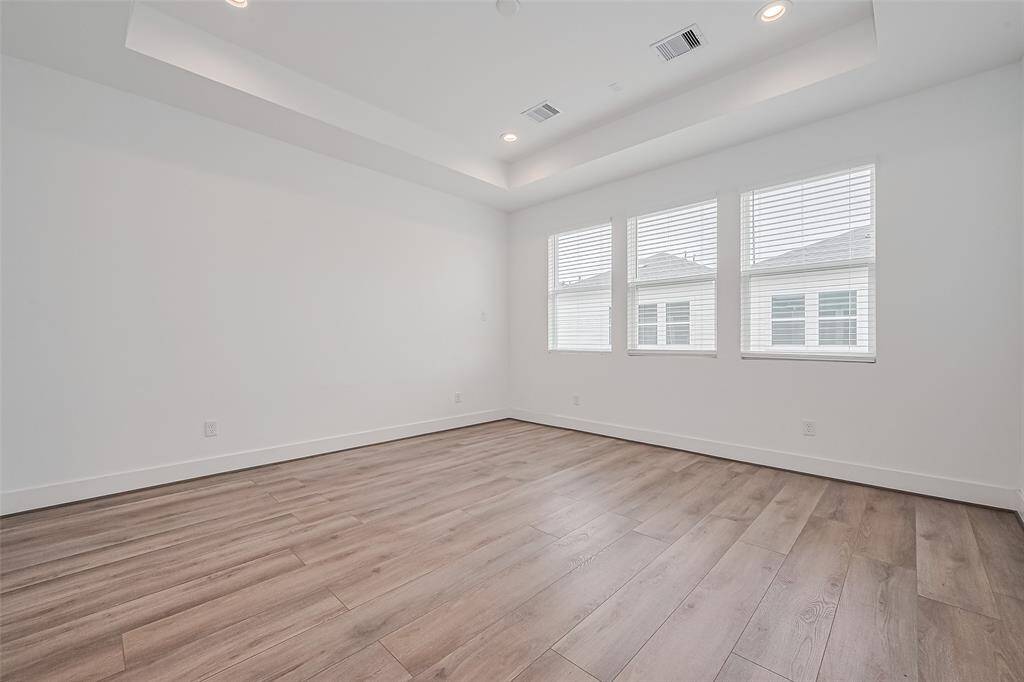 The primary bedroom is an expansive retreat featuring a tray ceiling, wide windows, and soft lighting that enhances the natural wood floors. A serene and spacious layout sets the tone for rest and renewal.