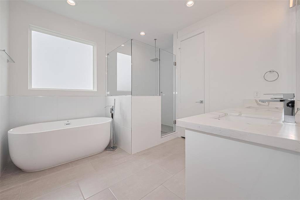 Unwind in the luxe primary bath with a soaking tub set beneath a frosted window, a glass-enclosed shower, and an expansive double-sink vanity. Clean lines, modern lighting, and generous storage create a spa-like ambiance.