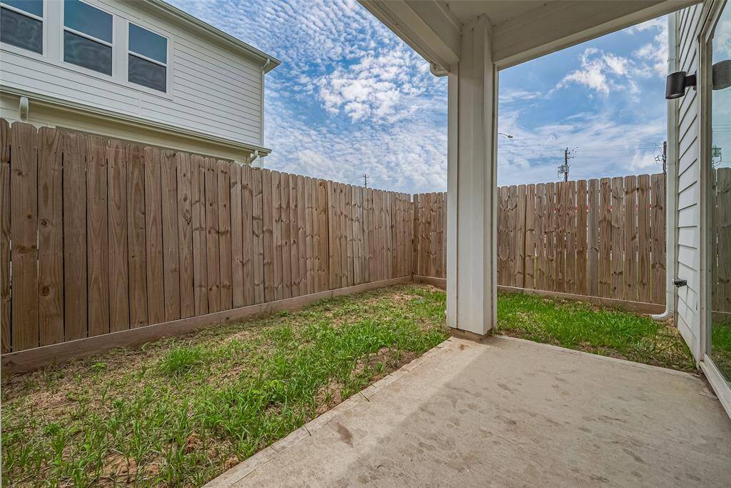 The covered patio extends the living space outdoors, with enough room for seating. It overlooks a grassy backyard, offering a private setting for relaxing or entertaining.