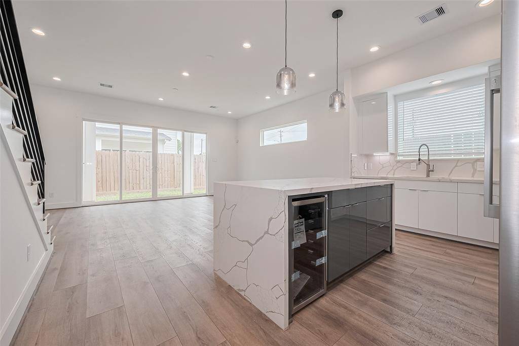 The kitchen and living space flow seamlessly in an airy open-concept design. A waterfall-edge quartz island provides a gentle division, enhanced by elegant pendant lights and layers of recessed lighting that create warmth and dimension.