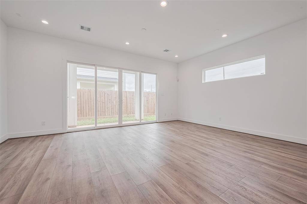 Anchored by warm-toned wood flooring, the spacious living room is bathed in natural light from sliding glass doors that lead to the backyard. A staircase with sleek lines adds architectural interest to the space.