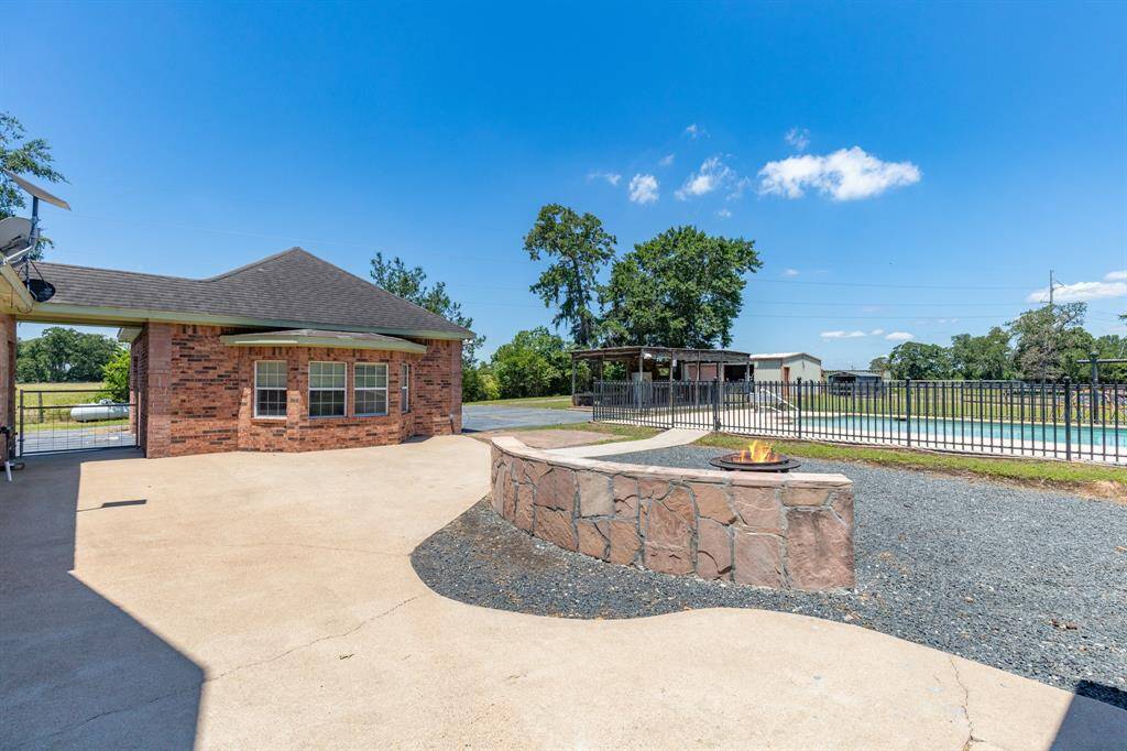 The yard includes a gravel section with a circular fire pit, surrounded by a low stone wall, and is enclosed by a fence, offering both functionality and privacy.