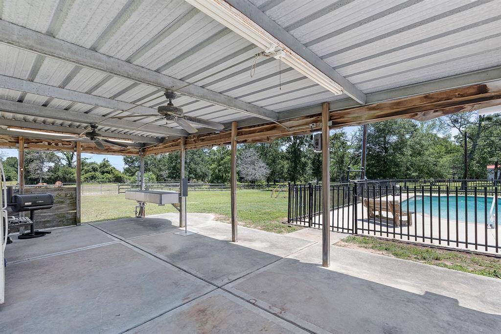 This photo showcases a spacious backyard with a brick house, featuring a large patio, a stone fire pit, and a fenced-in pool area. The setting is open and inviting, perfect for outdoor gatherings.