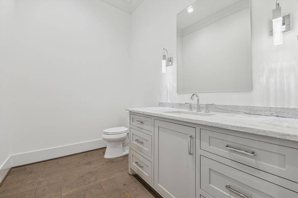 This powder bath features a spacious vanity with ample storage, sleek fixtures, and elegant finishes, all set against crisp white walls and warm wood flooring for a clean, modern look.
