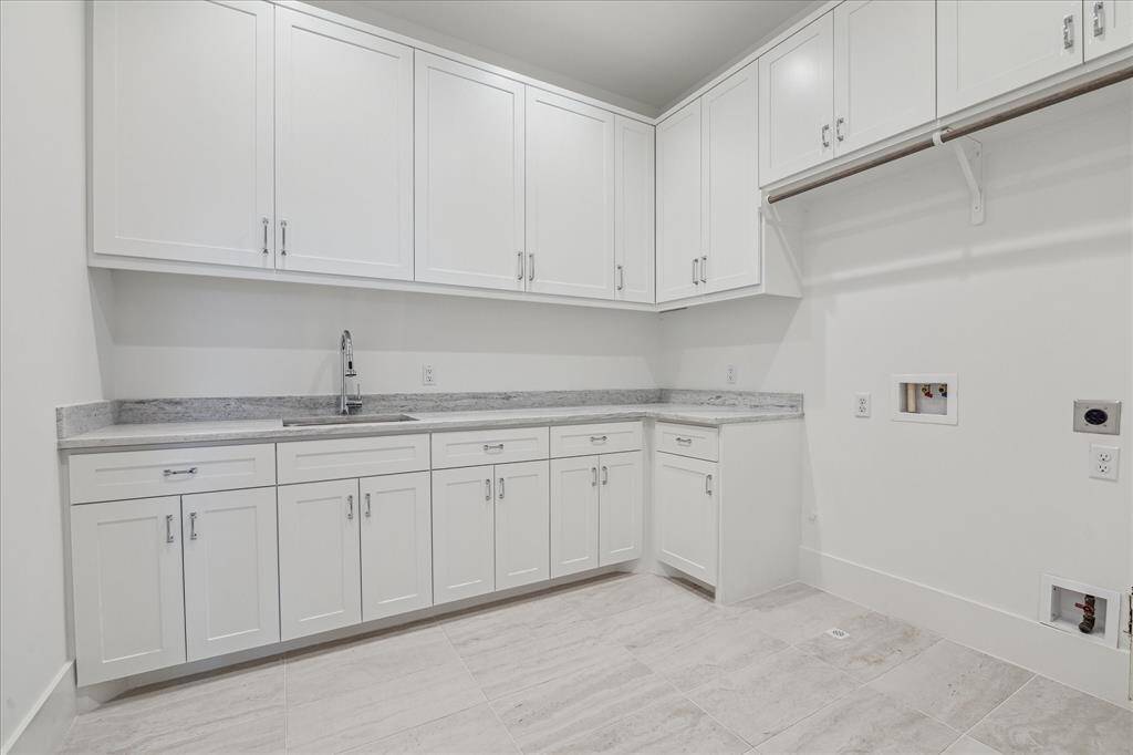 This spacious utility room features abundant cabinetry, ample counter space for folding, a built-in sink, and dedicated connections for laundry appliances, offering both function and efficiency.