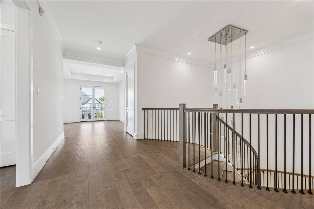 This second-floor landing features an open, airy design with wood floors, a sleek iron staircase railing, and a modern chandelier, complemented by French doors that open to a small balcony.