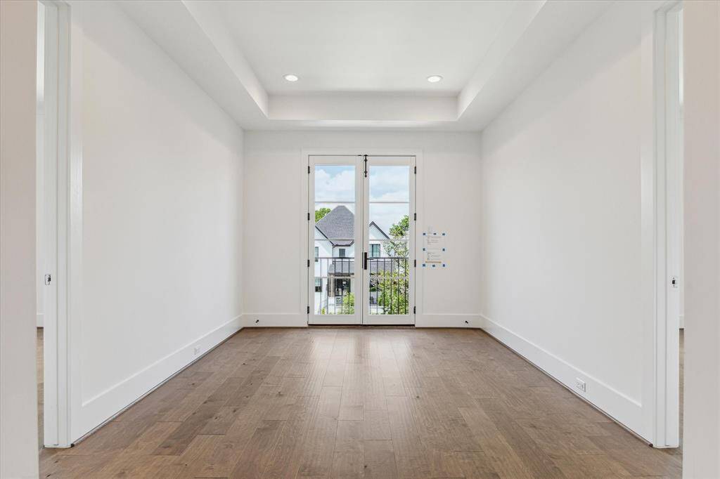 This bright upstairs hallway is accented by a tray ceiling, rich wood floors, and French doors that open to a Juliet balcony, bringing in natural light and adding an elegant architectural touch.