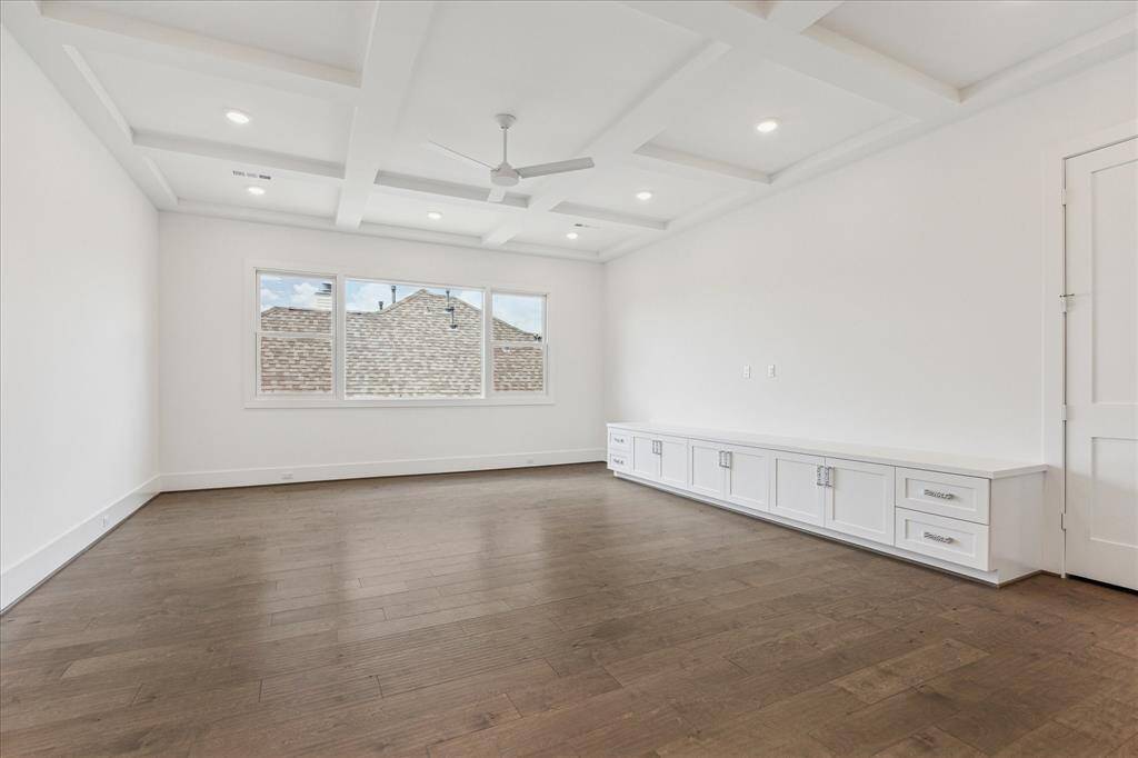 This spacious game room features a coffered ceiling, wood flooring, and built-in cabinetry along one wall, offering plenty of space for recreation, lounging, or media setup.