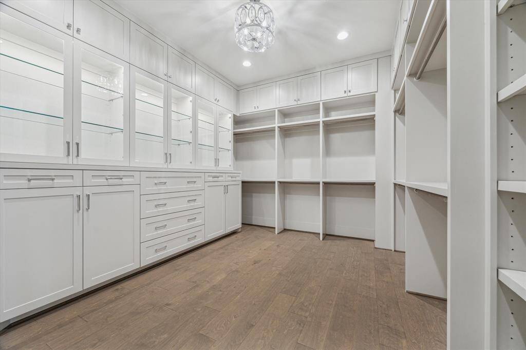 This expansive primary closet offers custom built-ins with glass-front display cabinets, ample drawers, and extensive hanging space, all designed to provide organized, boutique-style storage.